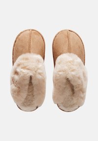 Chaussons en daim beige avec doublure en fausse fourrure crème moelleuse, forme arrondie et coutures contrastées le long des coutures. Texture douce.