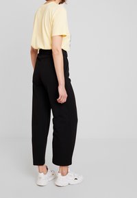 Černé kalhoty s vysokým pasem a zúženými nohavicemi, kombinované s světle žlutou košilí s krátkým rukávem. Nosí se s bílými teniskami. Hladká textilie.