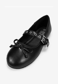 Ballerine en cuir noir avec un bout arrondi, dotée d'un nœud décoratif et d'une bride de cheville avec des œillets en métal et une boucle.