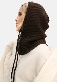 Brązowa prążkowana dziana kaptur z troczkami, z wysokim kołnierzem. Połączony z jasnym, teksturowanym okryciem wierzchnim.