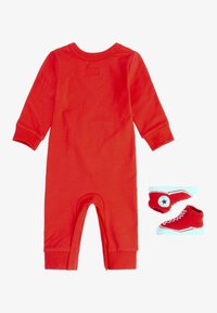 Rød fleece heldrakt med lange ermer og rund halslinning, kombinert med matchende røde tøfler med hvite såler og snørebånd.