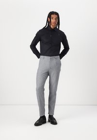 Black button-up shirt with long sleeves, gray textured trousers, and black dress shoes, featuring a modern fit and clean lines.