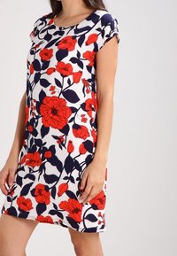 Vestido floral con patrones de flores rojas y marinas sobre un fondo blanco, de mangas cortas, cuello redondo y corte a la rodilla. Material de mezcla de algodón.
