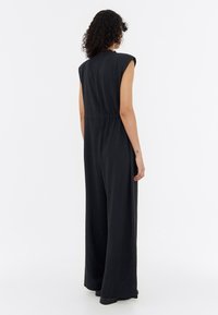 Black sleeveless jumpsuit with a cinched waist, wide-leg design, and smooth fabric, featuring subtle texture and no visible patterns or embellishments.