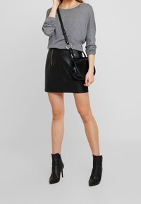 Harmaa pitkähihainen paita, musta nahkainen minihelma, musta olkalaukku ja mustat korkeat nilkkasaappaat. Yksinkertainen, vartalonmyötäinen muotoilu.