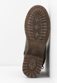 Brązowa gumowa podeszwa z deseń i logo, z zieloną tkaniną na górze oraz brązowymi skórzanymi akcentami na pięcie i szwach.