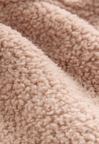 Blød, tekstureret stof i lys beige med en fyldig, dunet overflade. Materialet har en let glans og ujævne, fluffy mønstre.