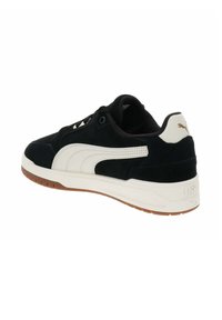 Zapatillas de ante negro con detalles en cuero blanco, suela de goma, cordones planos y un logo en el talón, con una base de goma marrón.