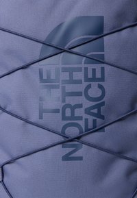 Blå stoffveske med et preget logo, med et kryssende elastisk design. Teksturert overflate og matt finish med ton-i-ton fargevalg.