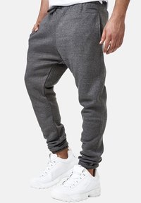 Gray sweatpants made of soft fabric, featuring an elastic waistband, side pockets, and tapered cuffs, paired with white sneakers.