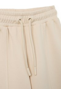 Beige Jogginghosen mit einem elastischen Bund und Zugbändern, weichem Material und gestickten Details an der Vorderseite.