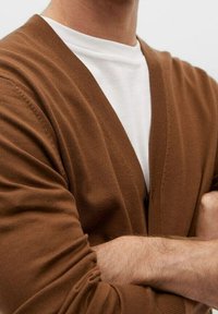 Cardigan marrone a maglia con scollo a V e apertura frontale. Indossato su una maglietta bianca a girocollo, mette in risalto una vestibilità comoda e una texture morbida.