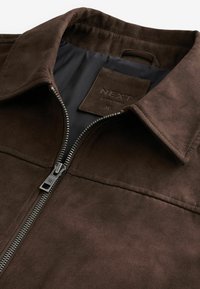 Brown suede jacket with silver zipper partially opened, showing black inner lining and "NEXT" brand label with size medium.