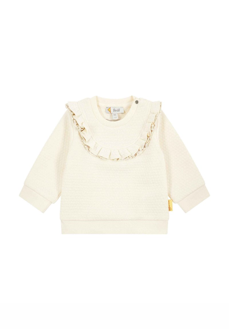 Sweatshirt pour enfants de couleur crème avec un tissu texturé, un col à volants et une chaîne décorative. Il possède des manches longues et des poignets côtelés.