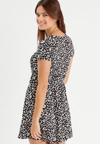 Schwarzes Kurzarmkleid mit weißem Blumenmuster, taillierter Oberteil und schwingendem Rock. Mit einem Band in der Taille für eine definierte Form. Glatte Stofftextur.