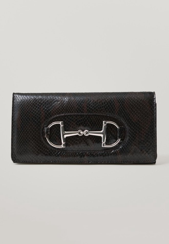 Portefeuille en cuir noir texturé avec un détail métallique argenté en forme de mors de cheval centré sur le rabat avant, sur fond uni.