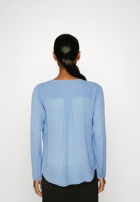 Camicia azzurro chiaro a maniche lunghe con design a pieghe sul retro, orlo arrotondato e polsini con bottoni. Texture liscia e vestibilità comoda.