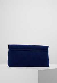 Bolso de mano de ante azul marino con forma rectangular, cierre de solapa y textura suave. Diseño minimalista sin acentos de hardware visibles.