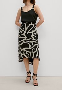 Zwarte satijnen camisole met verstelbare bandjes, gecombineerd met een zwart en crème abstract patroon midi rok en zwarte sandalen met bandjes.