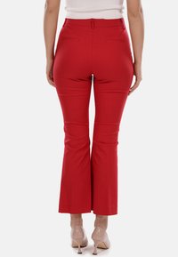 Pantaloni rossi svasati con una texture liscia, vita media e due tasche posteriori. Il taglio sartoriale esalta la silhouette. Abbinati a décolleté color carne.