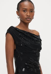 Melna kleita bez pleciem, izgatavota no mīkstas auduma, ar ziedu pērlīšu rotājumiem, drapēta dizaina un pieguloša silueta.