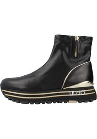 Stivale alla caviglia in pelle nera con chiusura a zip, accenti in metallo dorato e una suola a piattaforma stratificata con strisce dorate e nere.