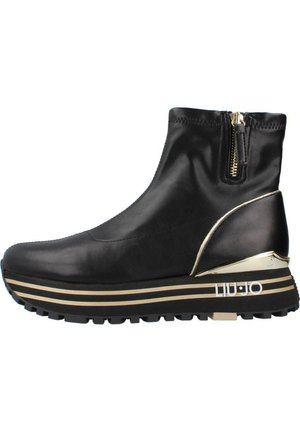 Stivale alla caviglia in pelle nera con chiusura a zip, accenti in metallo dorato e una suola a piattaforma stratificata con strisce dorate e nere.