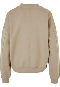 Beige hettegensere med ribbet rund hals, senkede skuldre og teksturert overflate. Har en sentral søm bak og mansjetterte ermer.
