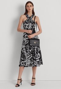 Abito midi floreale in bianco e nero con scollatura a halter, corpo aderente e gonna svasata, abbinato a una piccola borsa a tracolla nera e tacchi a strappy.