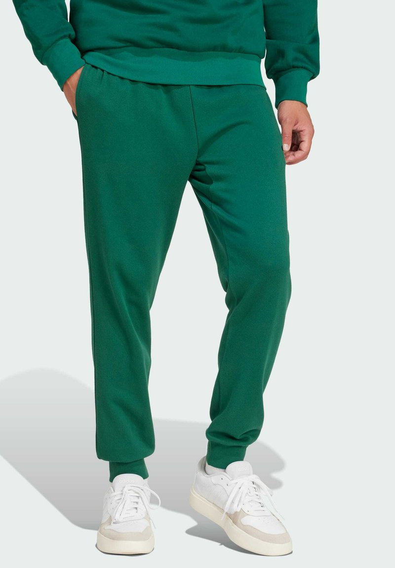 Pantalones de chándal verdes hechos de tela suave, con una cintura y puños elásticos. Combinados con zapatillas blancas. Textura suave, diseño ajustado.