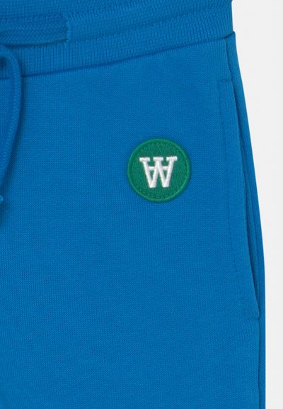 Calças de jogging azul em algodão com um patch circular verde com o logótipo branco "W", cintura elástica e bolsos laterais. Tecido suave e texturizado.