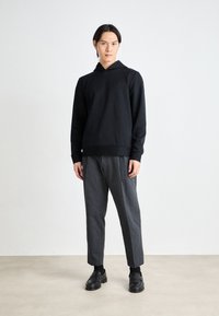 Un hoodie noir côtelé avec une poche frontale et une capuche à cordon, associé à un pantalon à rayures grises et des mocassins noirs. Texture lisse.