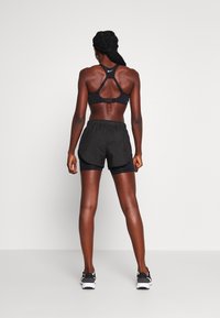 Sujetador deportivo negro con diseño de espalda nadadora, combinado con pantalones cortos deportivos negros que cuentan con una cinturilla elástica y forro interior.