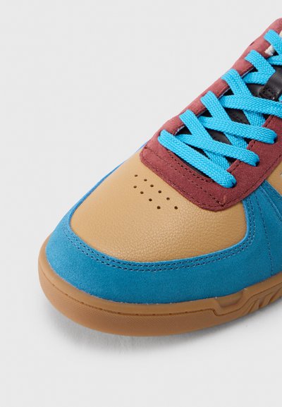 Ακροδάχτυλο αθλητικού παπουτσιού με δέρμα ταμπά, μπλε σουέτ διακοσμητικό, μαρον πάνελ με οπές και φωτεινά μπλε κορδόνια σε λείο λάστιχο σε γάλα καραμέλας πάνω σε λευκό φόντο.