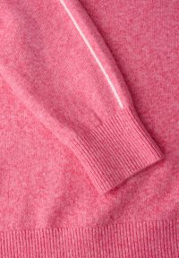 Różowy sweter z dzianiny o gładkiej fakturze, z prążkowanymi mankietami oraz kontrastującą białą paską na rękawie. Miękki i przytulny materiał.