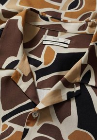 Hemd mit abstrahierter brauner, beiger, schwarzer und weißer giraffenähnlicher Musterung, ausgestattet mit einem Knopf und sichtbarem "Regular Fit"-Label.