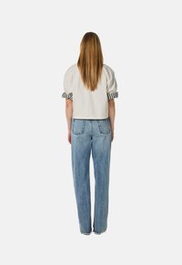 Afgeknot lichtbeige top met gestreepte manchetten, gecombineerd met high-waisted, loszittende blauwe denim jeans. Beide hebben een casual ontwerp.