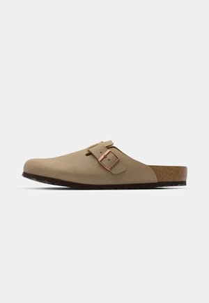 Beige clogs with a rounded toe, adjustable buckle accent, and cork footbed. Textured surface with a black rubber sole for grip.