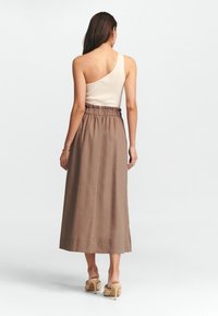 Beige rutig top med en axel, kombinerad med en lång brun kjol med elastisk midja och slät textur. Högklackade skor synliga.