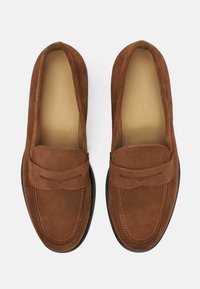 Smeđi mokasini oduated sa šavom na gornjem delu, ravnim đonom i dizajnom sa zaobljenim prstima. Unutrašnjost ima glatku podstavu.