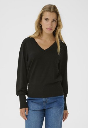 Maglione nero a V con maniche lunghe, texture morbida e polsini aderenti, abbinato a jeans in denim blu. Design semplice e classico.