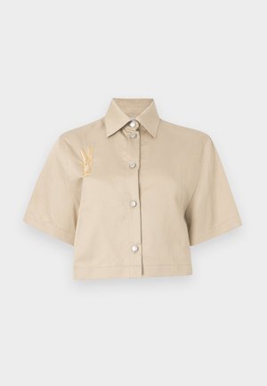 Sintetinė šviesiai smėlinė marškinė su trumpomis rankovėmis, priekiniais mygtukais ir sidabriniais mygtukais. Kairėje pusėje turi geltoną siuvinėtą detalę.