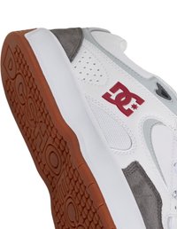 Bílé tenisky s šedými a červenými akcenty, s texturovanou gumovou podrážkou s rybinovým vzorem a perforovanými částmi po stranách.