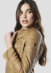 Hnedá kožená motocyklová bunda s prešívanými akcentmi na pleciach, so stojačikom a zipsovými vreckami. Jemné logo značky na rukáve.