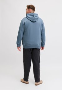 Μπλε φούτερ με κουκούλα από απαλό υλικό, με άνετη εφαρμογή. Συνδυάζεται με σκούρο γκρι παντελόνι και ανοιχτόχρωμα παπούτσια.