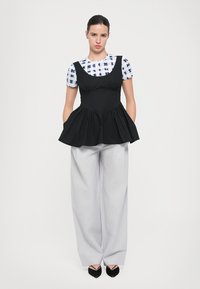 Top peplum fără mâneci de culoare neagră peste o cămașă cu model albastru și alb, asortat cu pantaloni cu picioare largi de culoare gri deschis și pantofi subțiri negri.