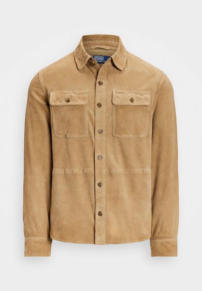 Tan suede button-up shirt with a collar, featuring two chest flap pockets and a straight hem. The texture is smooth and slightly shiny.