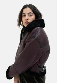 Burgunderrote Lederjacke mit schwarzem Kunstfellkragen, mit Reißverschluss und kontrastierenden schwarzen Akzenten. Strukturiertes Finish und taillierte Passform.