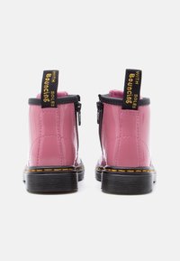 Ζευγάρι λαμπερών ροζ μποτάκια αστραγάλου με μαύρες σόλες, πλαϊνά φερμουάρ και μαύρες ταινίες έλξης με την επιγραφή "ΜΕ ΑΝΕΡΧΟΜΕΝΕΣ ΣΟΛΕΣ".