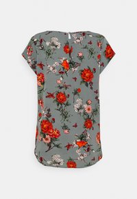 Blusa de manga corta floral en gris con patrones en rojo, rosa y verde. Presenta un escote redondo y un cierre con botón en la parte de atrás. Textura de tela suave.